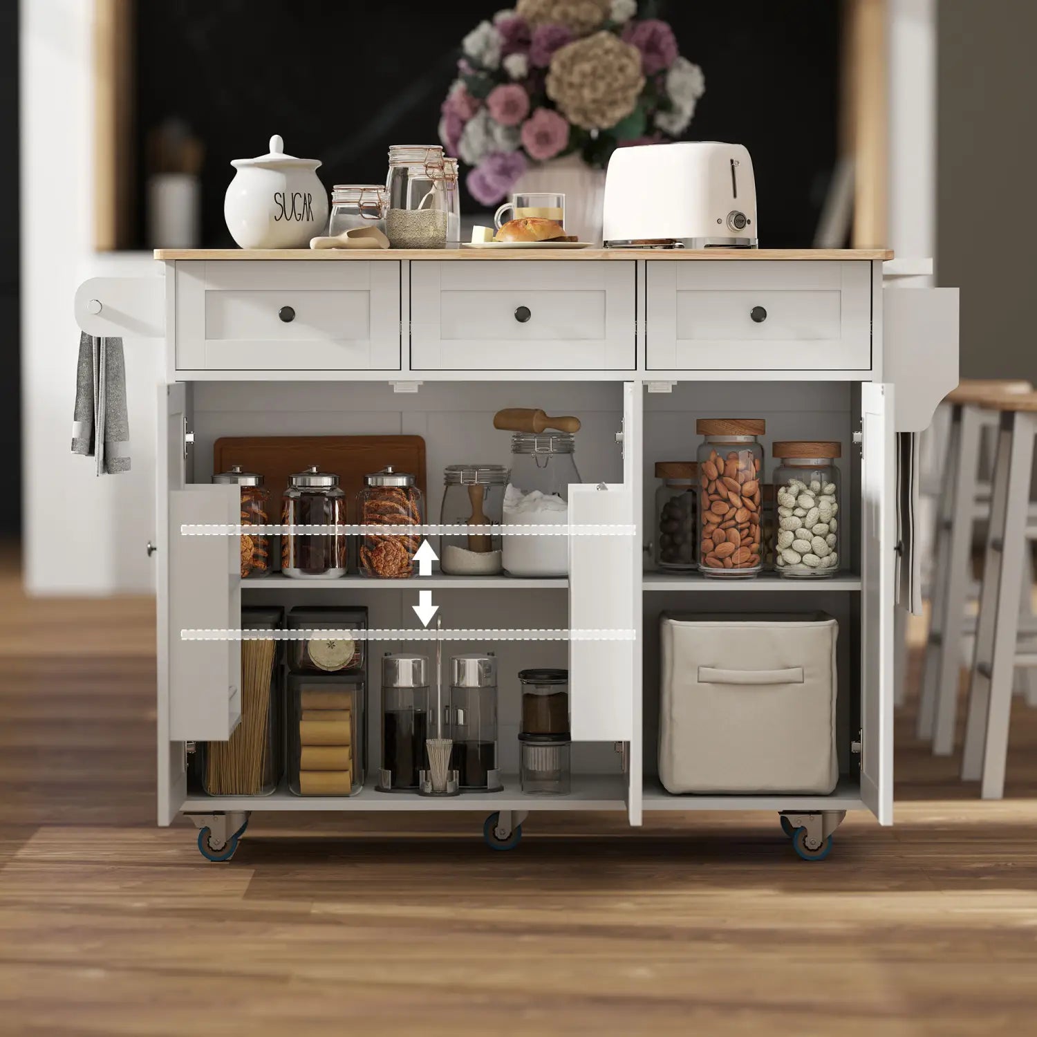 White kitchen island with drop leaf and charging station featuring a wooden countertop, three drawers, open shelving, and rolling casters for mobility.