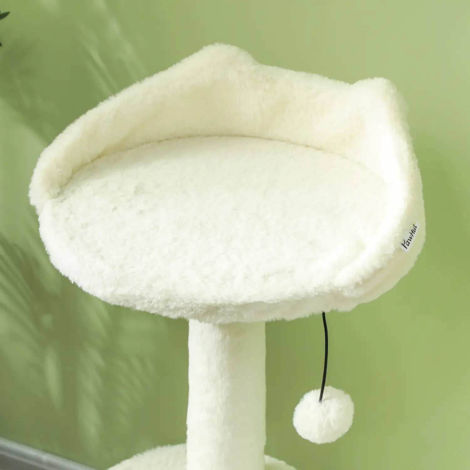 White fluffy cat bed made of soft plush material with a dangling pom pom toy in a cat tree tower with scratching posts and beds.