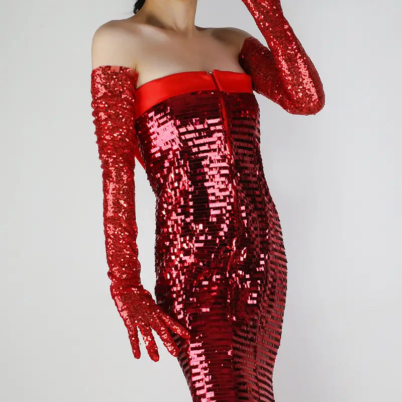 A dazzling red sequined off-the-shoulder dress with long matching mesh finger gloves and a satin belt at the waist in a form-fitting silhouette.