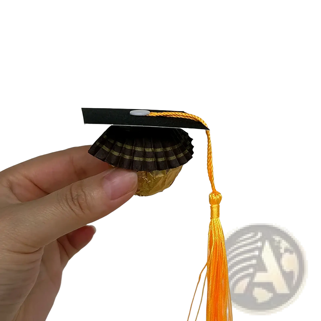 A 2025 graduation cap chocolate candy with a black paper top, gold foil base, and orange tassel decoration