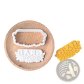 White plastic grad cookie cutter with floral design and yellow pressed dough sample from 2026 graduation cookie cutter set