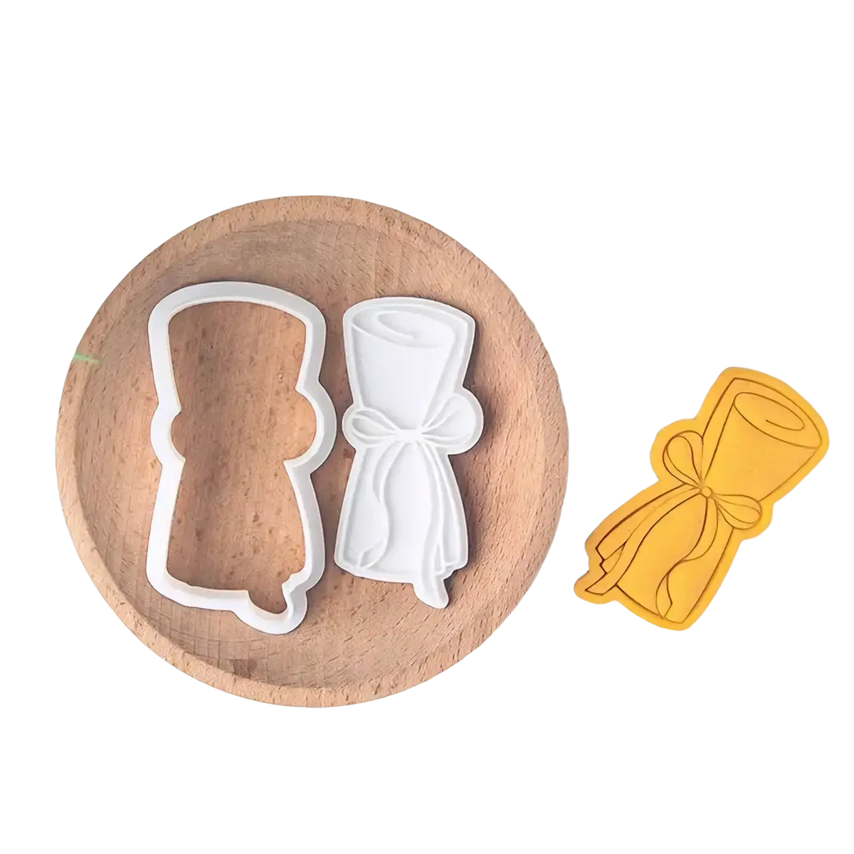 White plastic graduation cap and diploma cookie cutters on a wooden plate from the 2026 graduation cookie cutter set