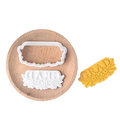 White plastic grad cookie cutter with floral design and yellow pressed dough sample from 2026 graduation cookie cutter set