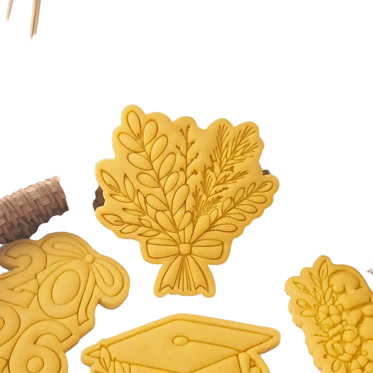Yellow plastic graduation cookie cutter with intricate leaf and bow design from 2026 graduation cookie cutter set