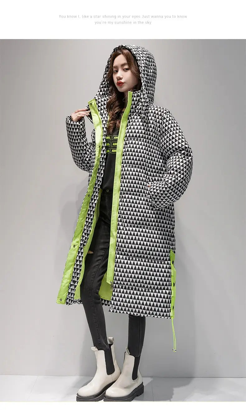 Un long manteau d’hiver à capuche en coton à carreaux pour femmes, avec un motif de triangles géométriques noir et blanc, une finition vert néon vive le long de la ligne de la fermeture et des coutures latérales.