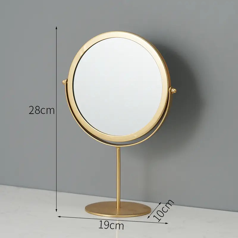 Gold-finished round vanity mirror with a metal frame, slender stand, and circular base for makeup desk use.