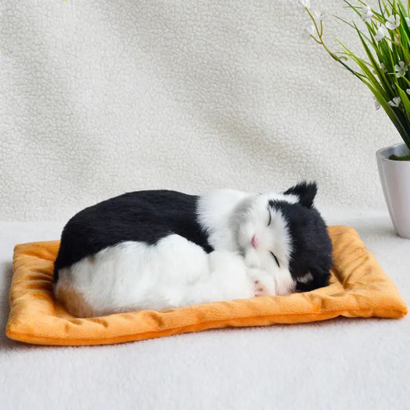 A realistic breathing plush black and white cat figurine sleeping peacefully on an orange pet bed cushion.