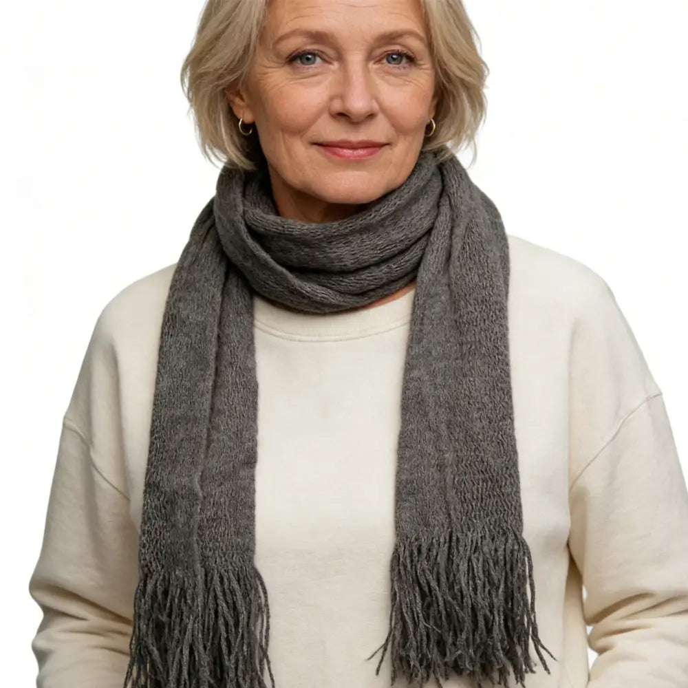 Une écharpe fine en acrylique tricotée, gris moyen, confortable, avec un tissage texturé et des extrémités frangées, accessoire d’hiver léger.