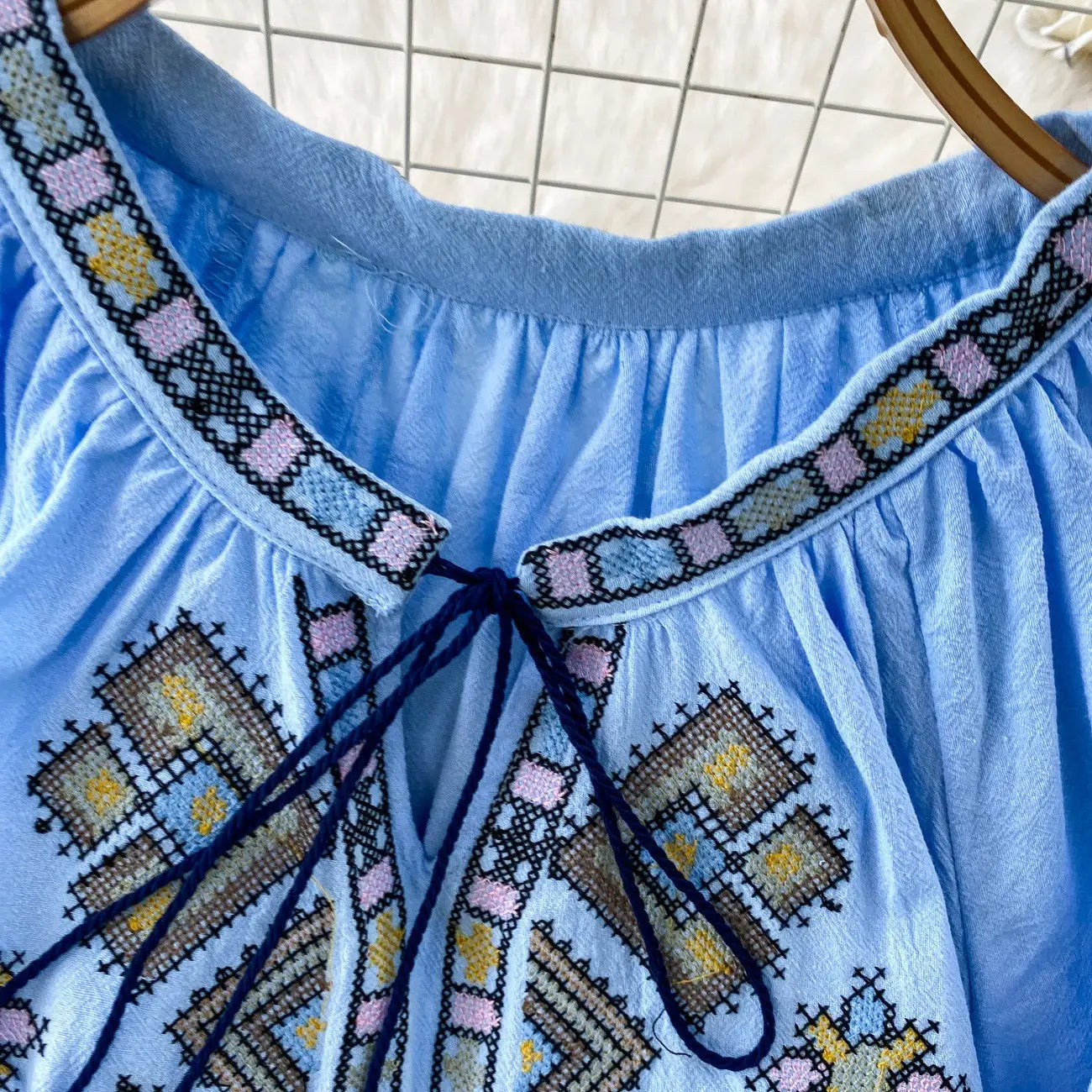 Light blue embroidered lantern sleeve tie neck blouse with ruffled collar and geometric patterns in pink yellow and black.
