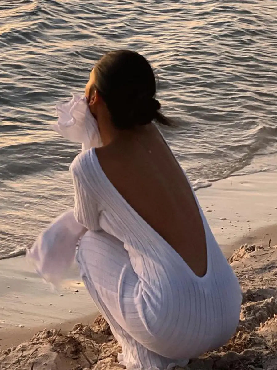 back view of a flowing white ribbed knit bodycon maxi dress featuring a deep back cutout and ruffled detailing