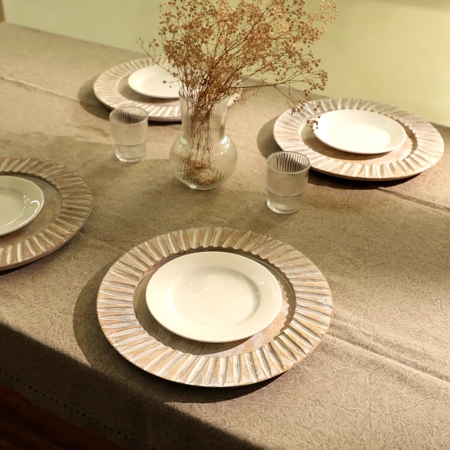 Assiettes en céramique blanches à bords festonnés reposant sur des sous-assiettes en bois texturé beige provenant de l’ensemble de sous-assiettes en bois artisanal blanc de 13 pouces.