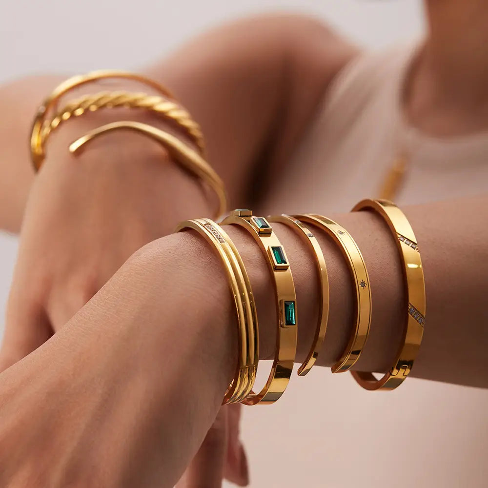 Gold plated stainless steel bangle bracelet featuring gold toned bangles with emerald green rectangular stones and diamond zirconia accents.