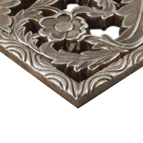 Antique bronze-colored metal trivet with intricate floral and leaf carvings complementing carved wood wall decor set distressed botanical panels.