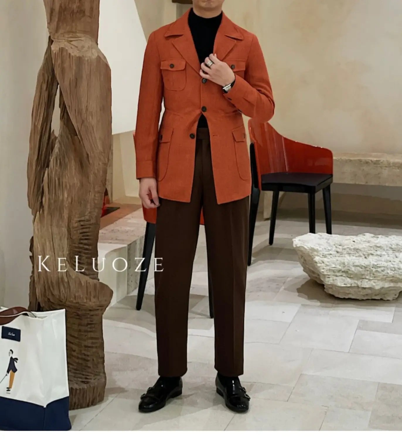 Un homme portant une veste de blazer double boutonnage ceinturée ajustée slim fit orange rouille, avec poches à rabat, associée à un pantalon marron foncé.