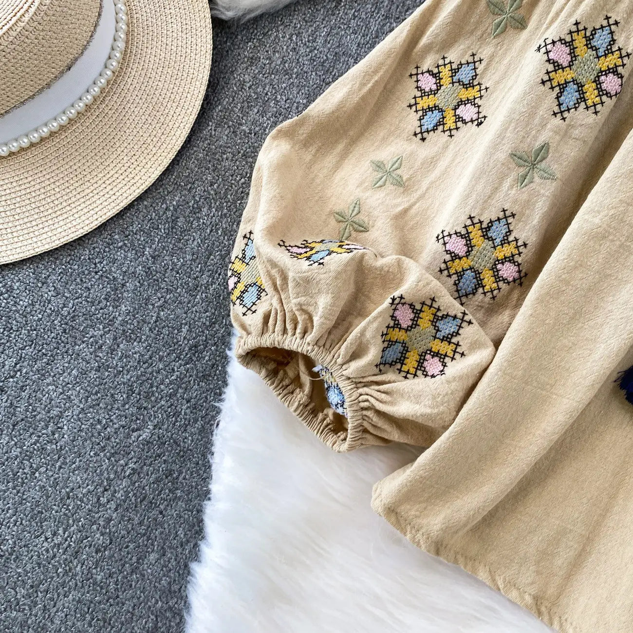 Beige linen dress with colorful cross-stitch embroidery in pastel shades of blue pink and yellow featuring embroidered lantern sleeves and a tie neck.