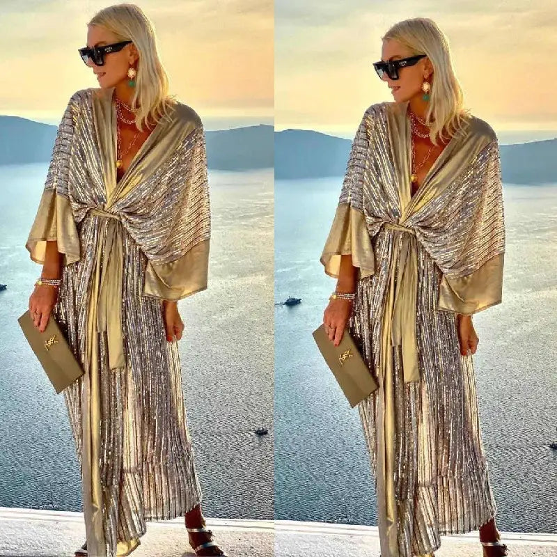 A shimmering gold sequined metallic bat sleeve pleated maxi dress with a draped tie-front design and wide sleeves.