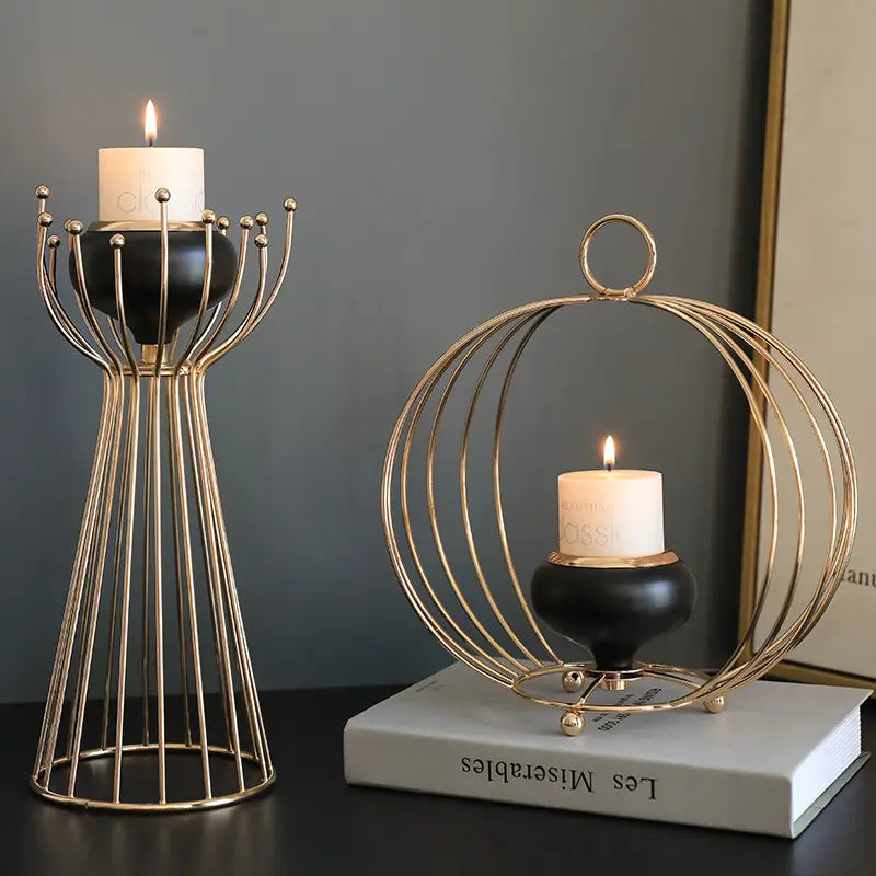Two elegant gold-toned metal geometric wire cage candle holders with black ceramic bases each holding a lit white pillar candle.