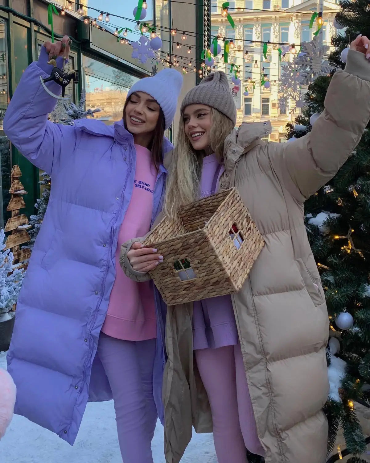 Un panier en osier tressé en forme de maison, avec une finition beige naturel et de petites ouvertures en forme de fenêtres, présenté à côté d’une doudoune matelassée à capuche pour femme, pour l’hiver.