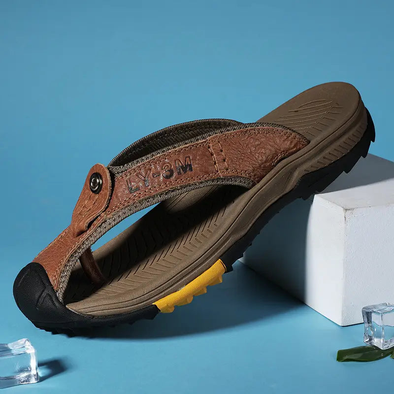 Men’s brown leather flip-flop with a rugged sole and yellow accent on the heel designed for outdoor beach sport use.