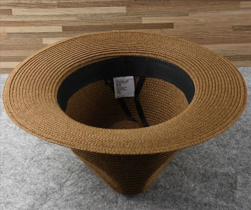 Tan straw fedora hat with black inner band and adjustable strap designed for foldable sun protection for men.