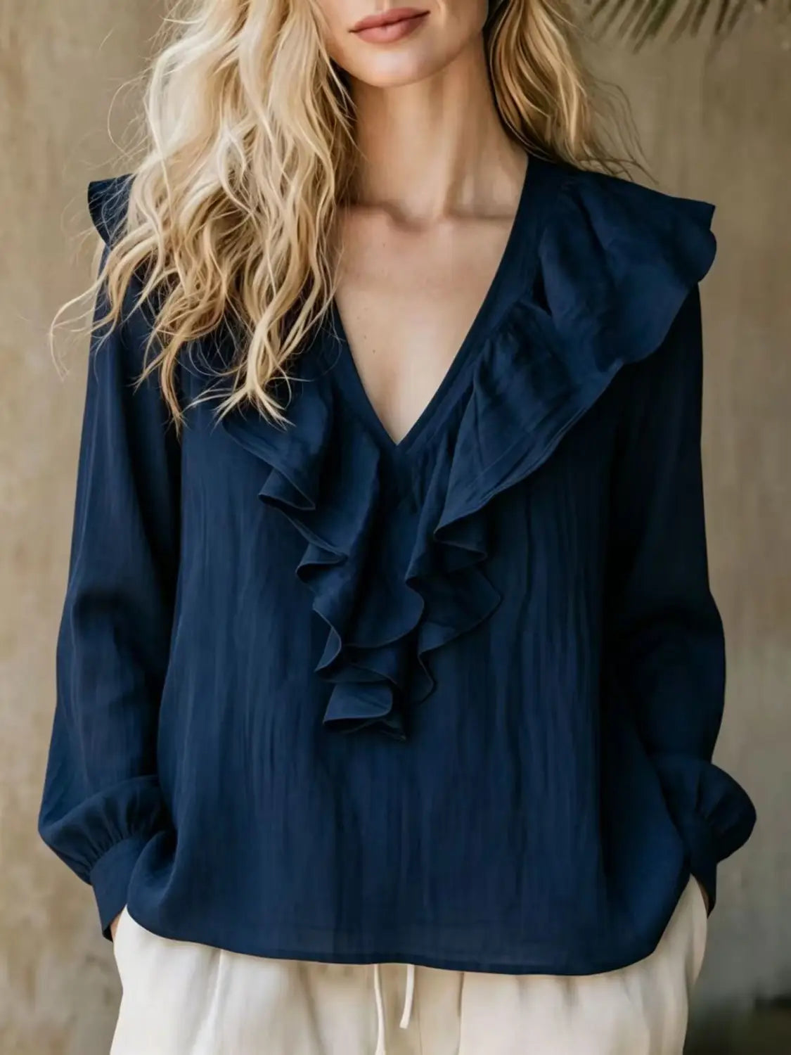 Une blouse en lin bleu marine à encolure en V et manches longues, avec des détails de volants et une conception légère.