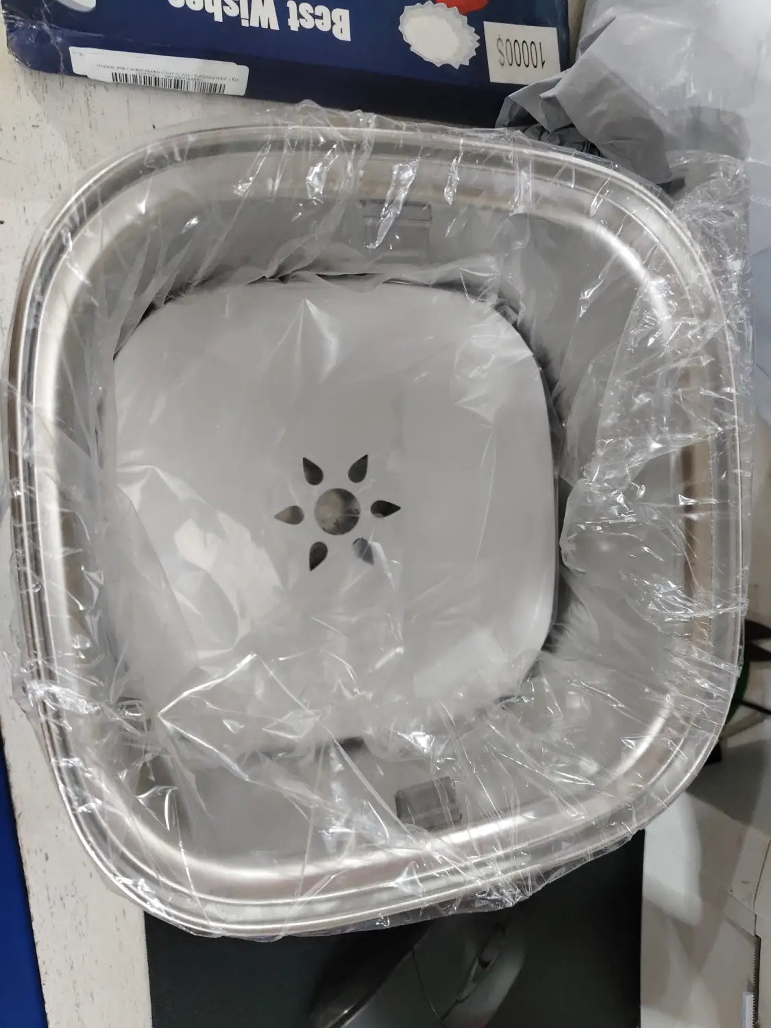 Gamelle flottante pour chien en acier inoxydable carrée, avec un couvercle de vidange central en forme d’étoile enveloppé dans un plastique transparent.