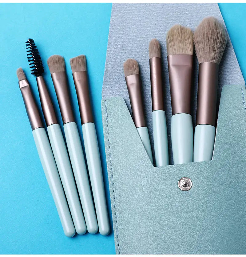 Makeup brush set with eight pieces featuring rose gold ferrules and light blue handles neatly arranged in a matching mint green leather case.