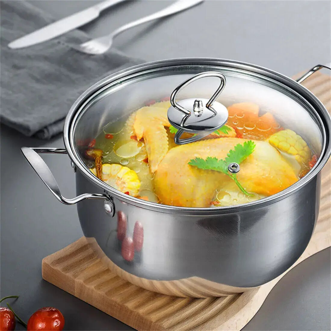 Stainless steel induction cookware set 11 pieces featuring a stainless steel pot with a clear glass lid and silver handle containing a cooked chicken dish garnished with cilantro.