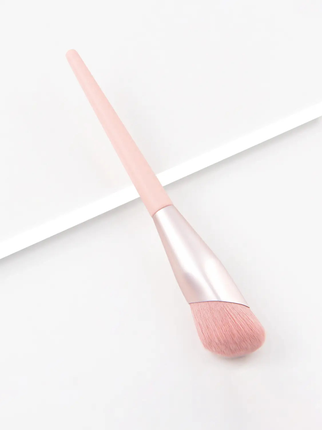 A soft pink finger belly makeup brush with a sleek metallic silver ferrule and matching blush-applying bristles designed for professional contour application.