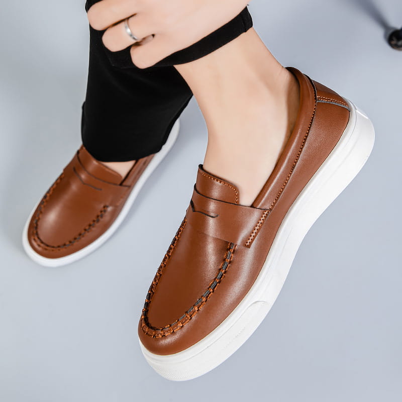 Mocasines marrones de cuero, tipo slip-on, con suelas de plataforma de goma blanca y costuras decorativas.