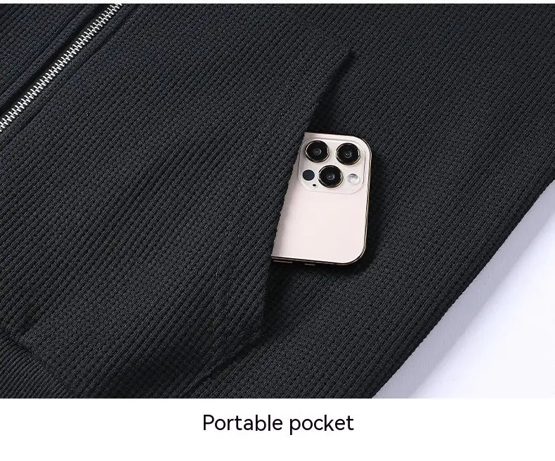 A sleek silver smartphone with a triple-camera array rests in the pocket of a black ribbed knit waffle hooded sportswear set.