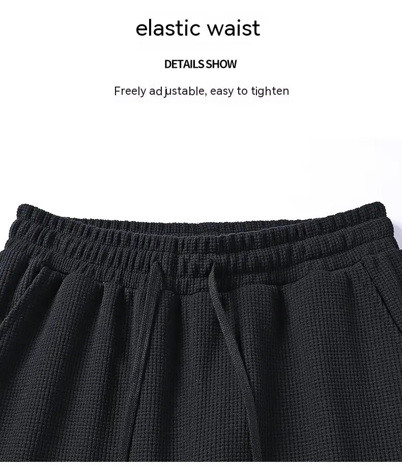 Black waffle-knit pants with elastic waistband and drawstring for adjustable fit in a waffle hooded sportswear set.
