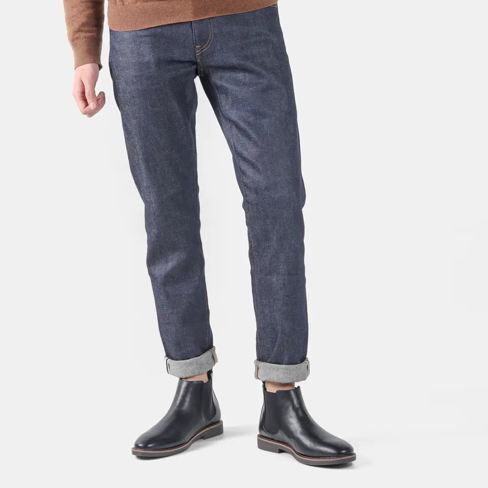 Herren wasserdichte Leder-Chelsea-Boots mit brauner Sohle, kombiniert mit schmal sitzender dunkel-indigoblauer Jeans mit umgeschlagenen Säumen.