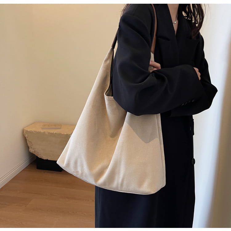 Beige canvas slouchy tote bag with a single suede shoulder strap and large capacity for versatile use.