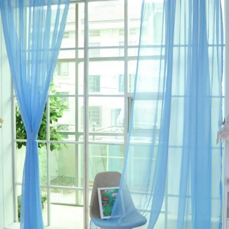 Light blue sheer tulle window curtains made of delicate fabric hang gracefully from a window gently filtering sunlight for living room and bedroom use.