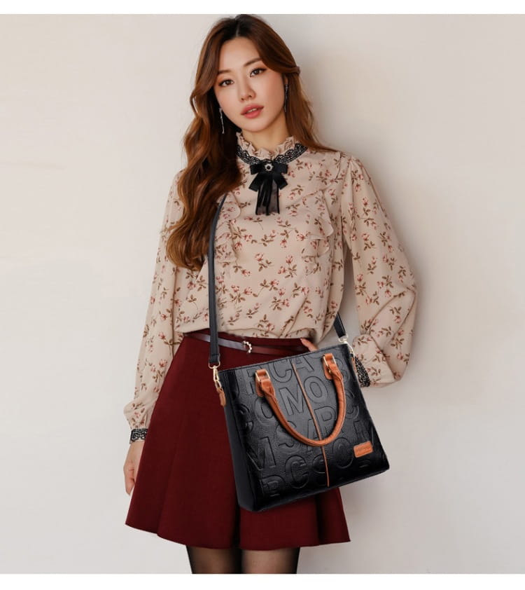 Black tote bag with tan leather handles and embossed leather detailing designed for large capacity carrying.