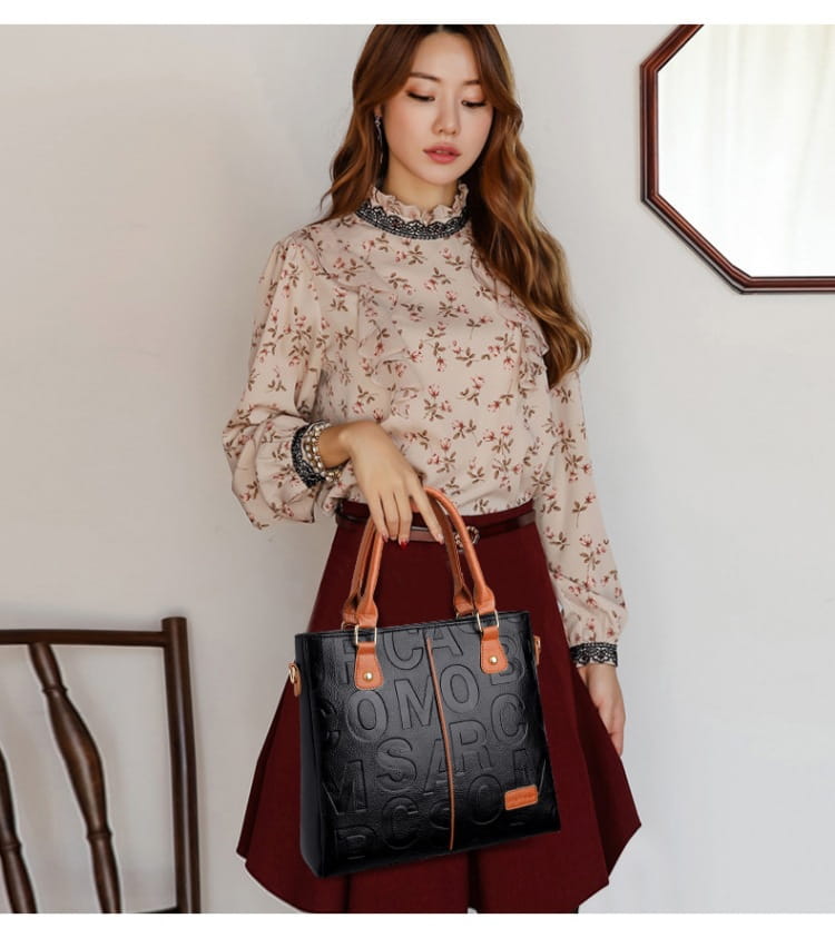 Black leather large capacity shoulder bag with tan handles and embossed lettering.
