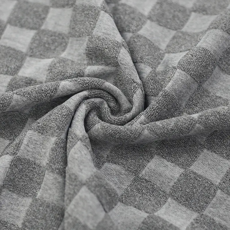 A soft plush gray and white checkered towel with a textured terry cloth weave accompanying a textured geometric cotton blend T-shirt and shorts set.