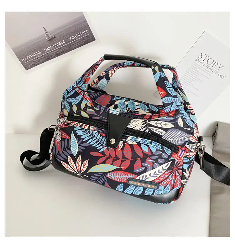 Oxford cloth floral messenger bag featuring a vibrant leaf pattern with a dark navy base and colorful red, blue, and green foliage design.
