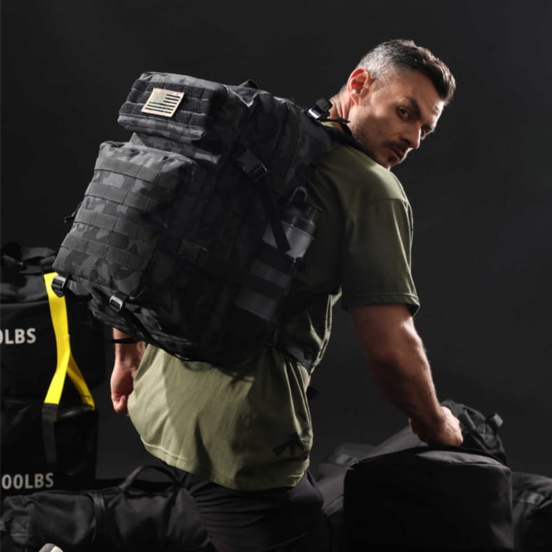 Black camouflage tactical backpack with a small American flag patch on the top flap designed for large capacity outdoor hiking use.