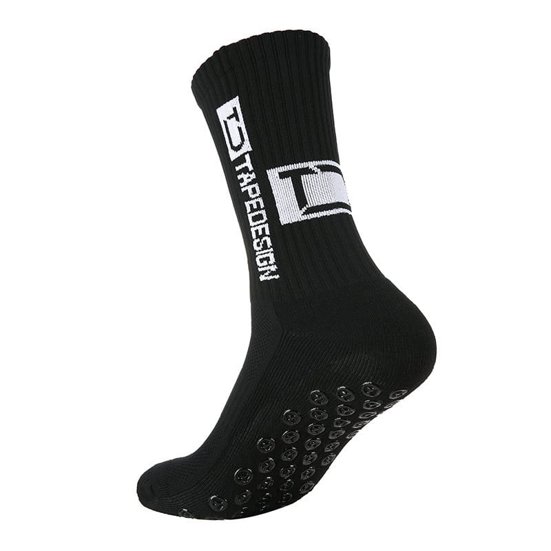 Chaussettes de football antidérapantes noires avec manchette côtelée, logo tapedesign blanc sur ruban et pastilles de caoutchouc rondes texturées sur la semelle.