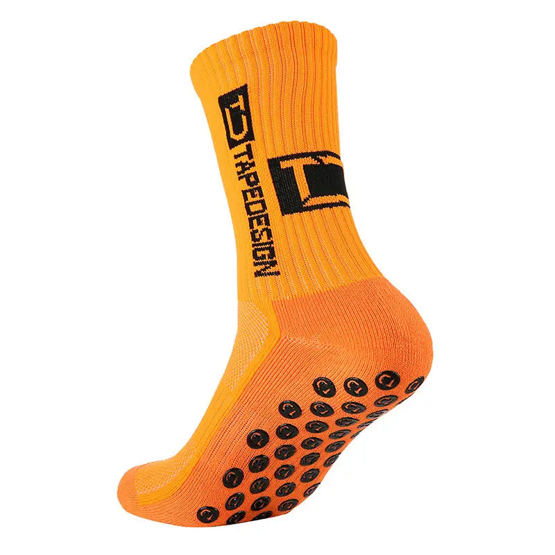 Chaussettes de football antidérapantes orange vif dotées de pastilles de caoutchouc circulaires noires sur la semelle et d’un logo de design trapèze noir au niveau de la manchette.