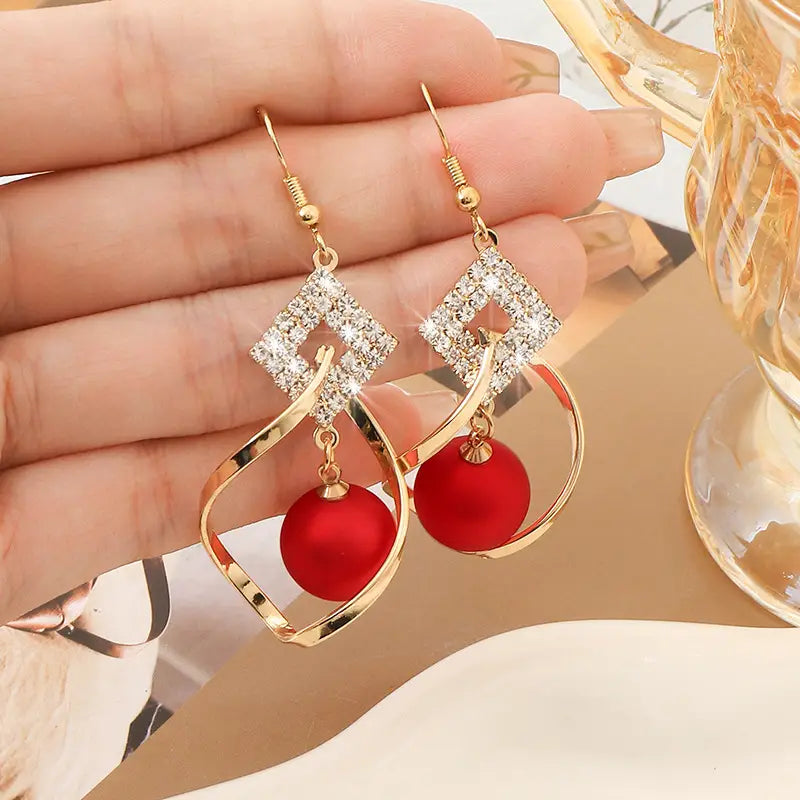 Rote Perlen- und Kristall-geometrische Gold-Tropfenohrringe mit goldfarbenem Tropfen-Design, quadratischen Oberteilen mit Diamantbesatz, geschwungenen Metallrahmen und herabhängenden roten Satin-Kugeln.