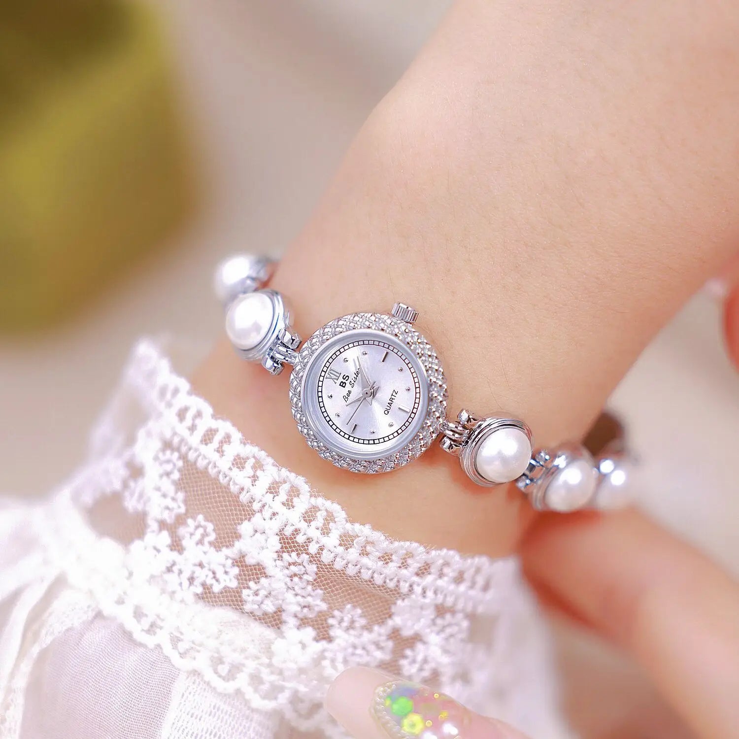 Elegant pearl bracelet quartz watch for women featuring a delicate silver-toned round face encircled by sparkling crystals and adorned with white pearls on the bracelet with minimalist black hour markers.