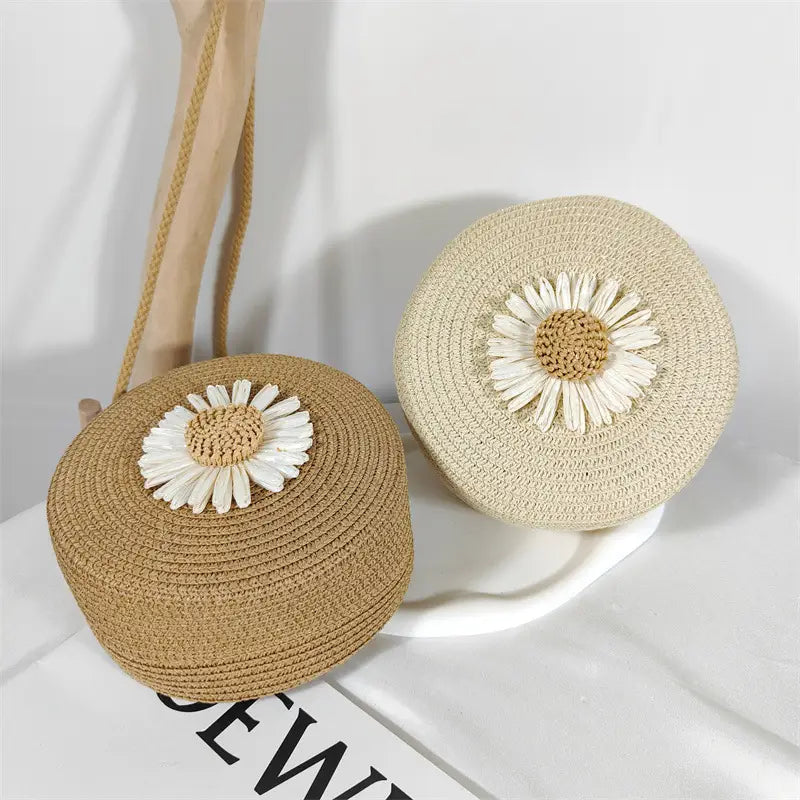 Beige woven straw round crossbody bag with a white daisy embellishment featuring a shoulder strap for casual use.