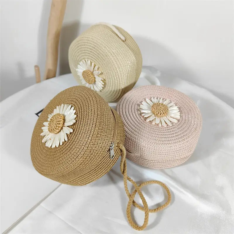 three round straw crossbody bags in beige tan and blush pink with white daisy embellishments displaying the daisy straw crossbody bag round woven shoulder purse design
