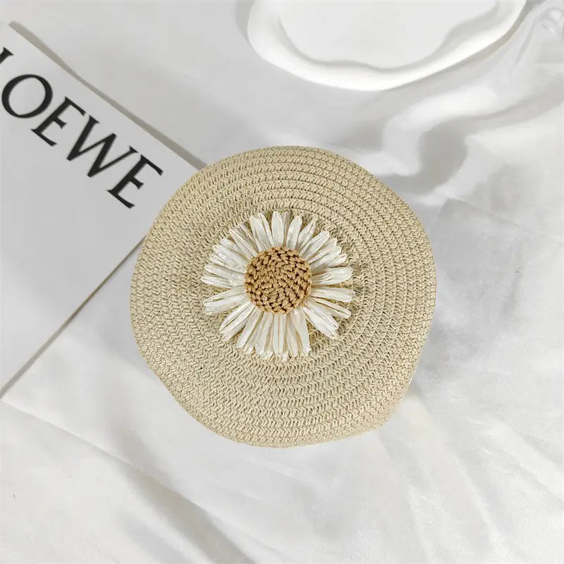 Beige woven straw round crossbody bag adorned with a white daisy embellishment designed as a shoulder purse.