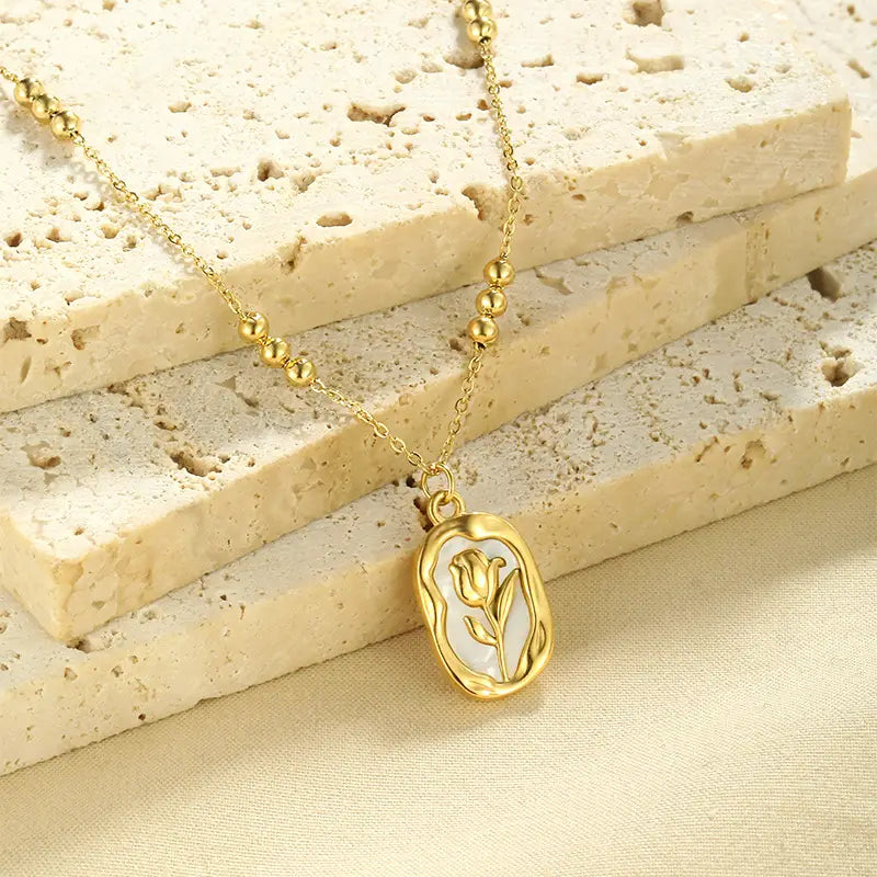 Gold-toned 18k gold plated stainless steel necklace with a delicate beaded chain and an oval tulip shell pendant inlaid with white material.