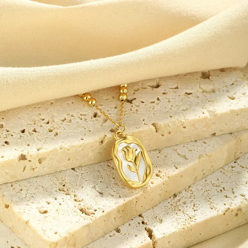 18k gold plated stainless steel necklace featuring an oval gold-toned pendant with a delicate tulip design inlaid on white enamel.