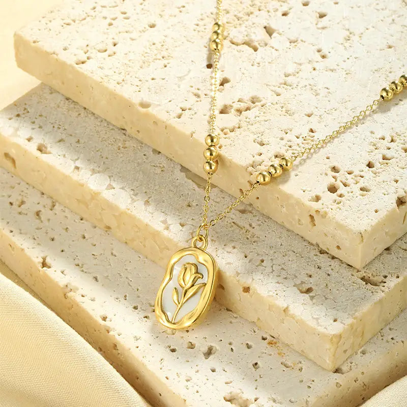 18k gold plated stainless steel necklace with an oval pendant featuring a delicate tulip shell design against a textured stone background.